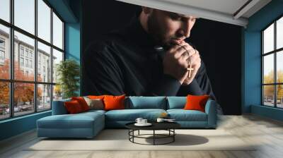 Young priest praying to God on dark background Wall mural