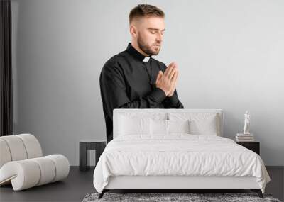 Young priest praying to God on light background Wall mural