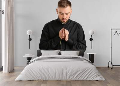 Young priest praying to God on light background Wall mural