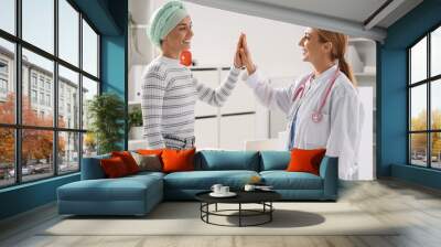 Young woman after chemotherapy with doctor giving each other high-five in clinic Wall mural