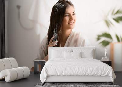 Young woman applying cream on beautiful long hair in bathroom Wall mural