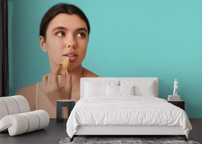 Young woman applying lip balm on color background Wall mural