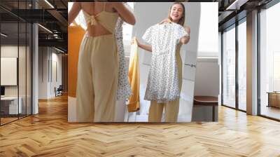 Young woman choosing clothes in front of mirror at home Wall mural