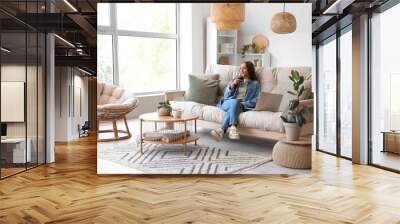 Young woman drinking wine on couch in living room Wall mural