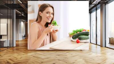 Young woman eating healthy vegetable salad in kitchen. Diet concept Wall mural