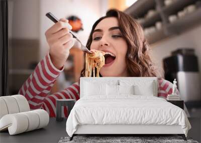 Young woman eating tasty pasta at home Wall mural