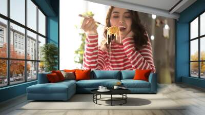 Young woman eating tasty pasta at home Wall mural