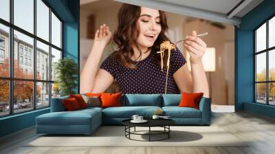 Young woman eating tasty pasta at table Wall mural