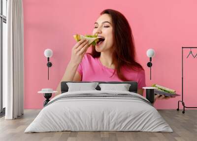 Young woman eating tasty sandwich on color background Wall mural