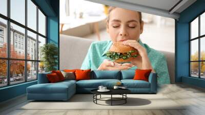 Young woman eating tasty vegan burger at home Wall mural