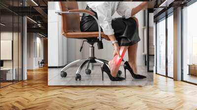 Young woman feeling pain in ankle at workplace in office Wall mural