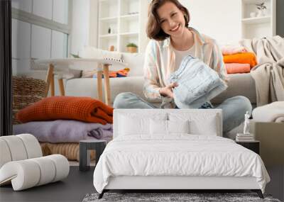 Young woman folding different clothes on floor at home Wall mural