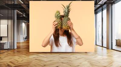 Young woman hiding face behind two pineapples on color background Wall mural