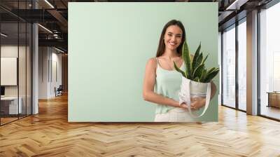 Young woman holding eco bag with houseplant on green background Wall mural