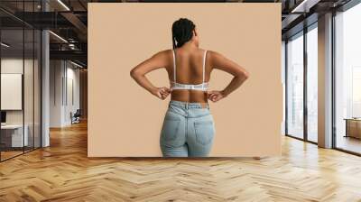 Young woman in bra on beige background, back view Wall mural