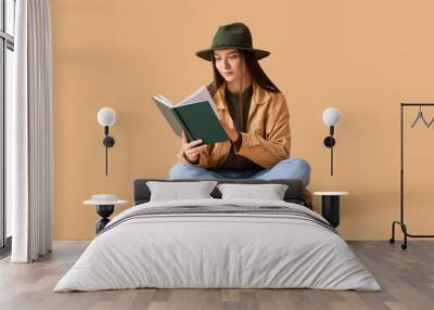 Young woman in hat reading book on beige background Wall mural