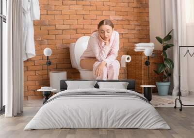 Young woman in pajamas sitting on toilet bowl in bathroom Wall mural