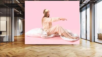 Young woman in pajamas with blanket and pillow on pink background Wall mural