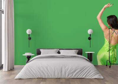 Young woman in stylish green dress dancing on color background, back view Wall mural