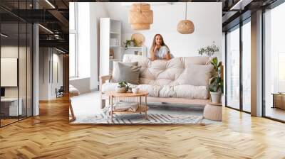 Young woman leaning on couch in living room Wall mural