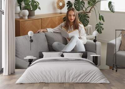 Young woman reading book on couch in living room Wall mural