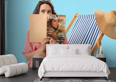 Young woman reading magazine in deck chair on blue background Wall mural