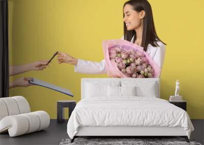 Young woman receiving bouquet of beautiful roses on yellow background Wall mural