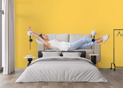 Young woman relaxing on sofa against color background Wall mural