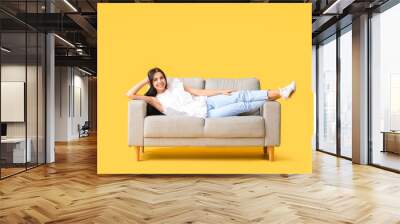 Young woman relaxing on sofa against color background Wall mural