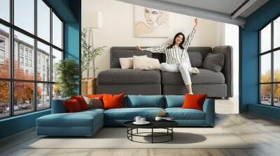 Young woman resting on black sofa in living room Wall mural