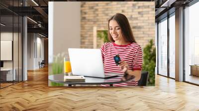 Young woman shopping online with credit card and laptop in cafe Wall mural