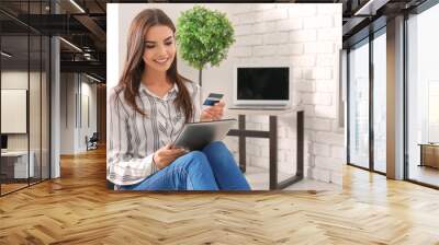 Young woman shopping online with credit card and tablet PC at home Wall mural