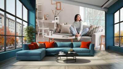 Young woman sitting on grey couch in living room Wall mural