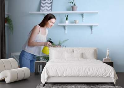 Young woman spraying water on houseplant at home Wall mural