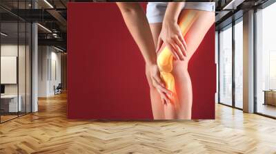 Young woman suffering from pain in knee on color background Wall mural