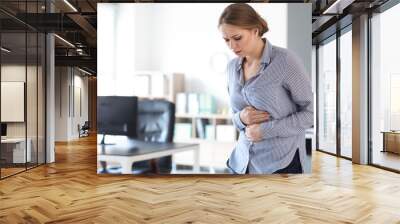 Young woman suffering from stomachache in office Wall mural