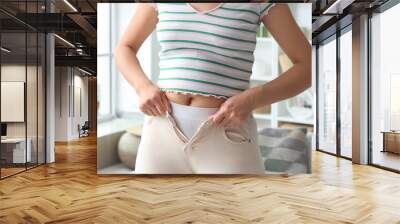 Young woman trying to button tight pants at home, closeup. Diet concept Wall mural