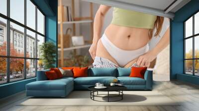 Young woman trying to put on tight jeans in bedroom, closeup. Weight gain concept Wall mural