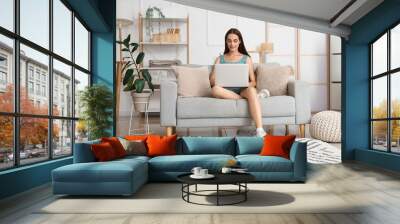 Young woman using laptop on grey sofa in light living room Wall mural