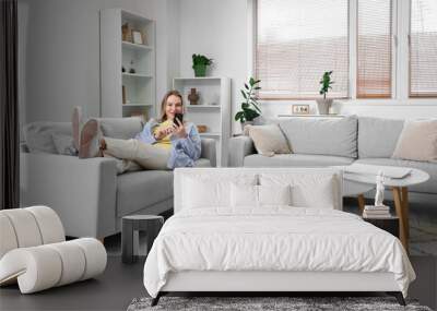 Young woman using mobile phone on sofa in light living room Wall mural