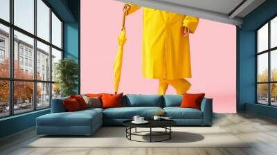 Young woman wearing yellow raincoat and gumboots with umbrella on pink background Wall mural