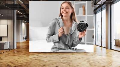 Young woman with cup of coffee and alarm clock on bed at home Wall mural