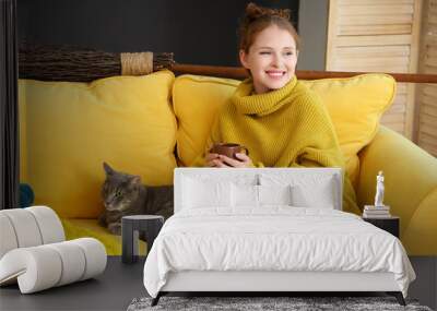 Young woman with cup of tea and cute cat on sofa at home Wall mural