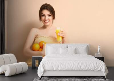 Young woman with glass of juice and oranges on beige background Wall mural