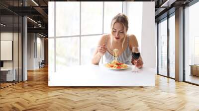 Young woman with glass of wine eating tasty pasta at table in restaurant Wall mural