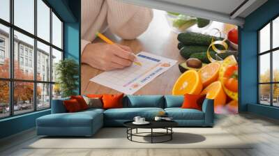 Young woman with healthy food making meal plan on table in kitchen, closeup. Diet concept Wall mural