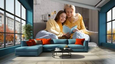 Young woman with her mother reading book at home Wall mural