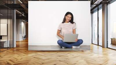 Young woman with laptop sitting on floor near light wall Wall mural