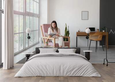 young woman with magazine sitting in comfortable armchair at home Wall mural