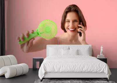 Young woman with mini green electric fan using mobile phone on pink background Wall mural